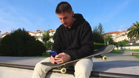 Close-Up of a Skater Sitting on the Half Pipe Edge, Texting on His Smartphone Stock Footage 285765945