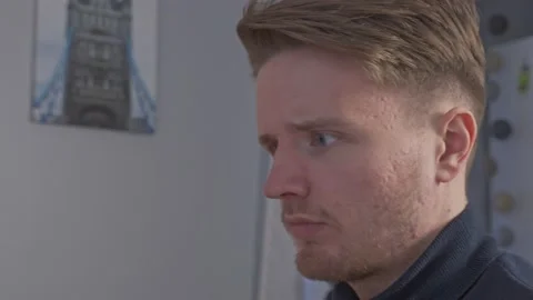 A close-up of a skeptical young man as he sits down at his desk trying to Stock Footage 205175078