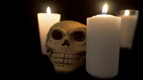 Close up to a skull and two candles light off in a black backgrond Stock Footage 96664449