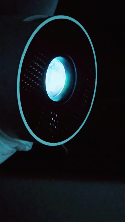 Close-up of a sleek modern mini projector lens glowing with bright cyan light Stock-Footage 345768042