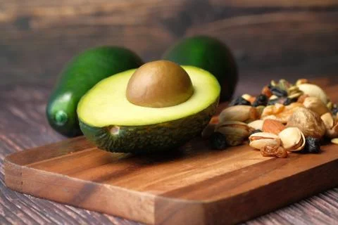 Close up of slice of avocado and mixed nut on chopping board. Stock Photos