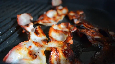 Close-up of a slice of bacon fried on a hot grill. Video stock 88868859