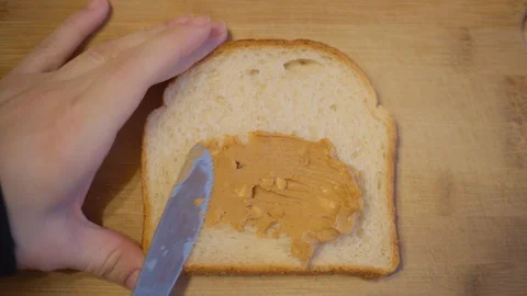 Close up slice of bread and knife smearing of peanut butter. Top view Stock Footage 127977212