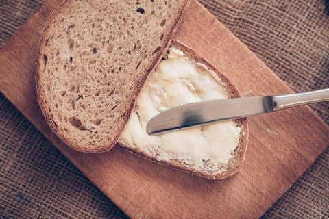 Close-up slice of bread with butter and knife on the wooden desk, poverty Фото