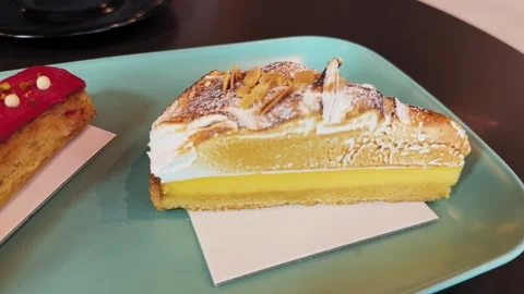Close-up of a slice of lemon cake with cream and almond flakes on a table in a Stock Footage 330287980