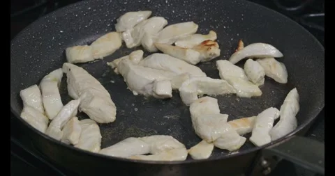 Close-Up of Sliced Chicken Breast Strips Sizzling and Sautéing in a skillet Stock Footage 322074576