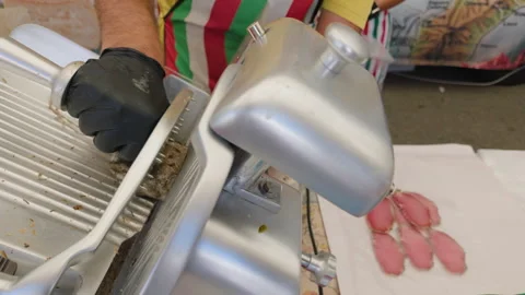Close-up of sliced deli meat on paper beside a meat slicer at a market stall, Stock Footage 344829057