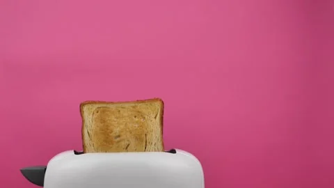 Close-up of sliced fried white bread flying out of an electric toaster on a pink Stock Footage 235396704