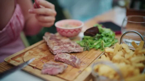 Close-up of a sliced medium-rare steak on a wooden board with fries, green salad 動画素材 348083349