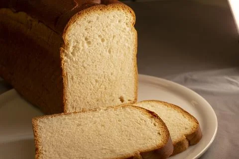 Close up sliced white bread loaf on plate under warm fresh light Stock Photos