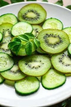 Close-up slices of kiwi and cucumber with leaf on white plate and rustic back Stock Photos