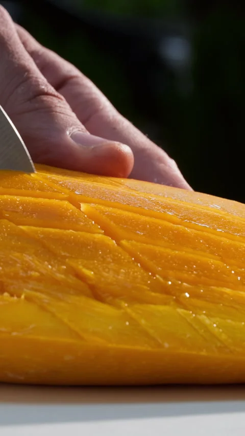 Close-up slicing fresh mango on cutting board on greenery background. Outdoor Stock Footage 314004791