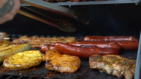 Close up slide right shot of man roasting juicy sausages and meat on grill and Stock Footage 136735702