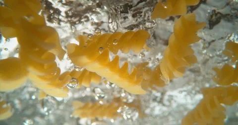Close up slow motion of fusilli pasta falling into boiling water and cookin.. Stock Footage 337418788