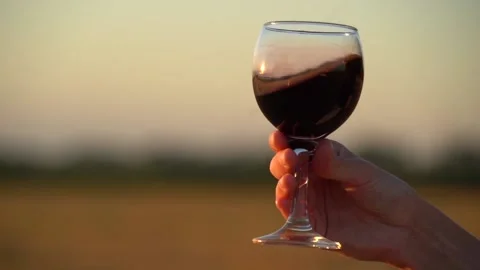 Close up. Slow motion. Glass of red wine in hand of girl against a sunset. Stock Footage 135542888