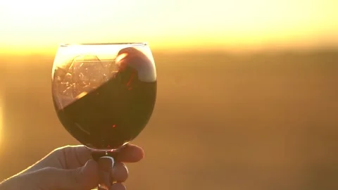 Close up. Slow motion. Glass of red wine in hand of girl against a sunset. Video stock 135542905