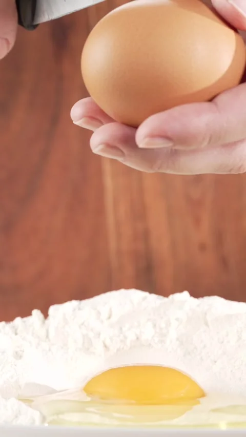 Close-up slow motion of hands breaking an egg into flour with another egg a.. Video stock 312168874