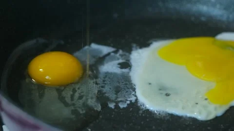 Close-up slow motion hands cracking egg in hot skillet, fried egg beginning form Video stock 312984062