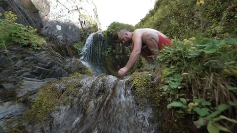 CLOSE UP, SLOW MOTION: Hiker stops to wash his face with the glassy river water Vidéo 121860015