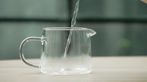 Close up slow motion pouring hot boiling water into transparent glass kettle on Stock Footage 295033178