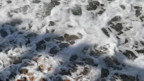 Close up slow motion of sea wave breaking on pebble beach with foam and colorful Stock Footage 341452456