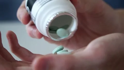 Close-up slow motion shot of white pills being poured into a hand against Video stock 317049082