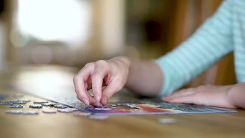 Close-up slow motion view of young woman hands assembling puzzles at home. 스톡 동영상 319637770