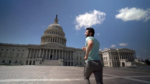 Close up slow motion of young man jumping for joy in front of the US Capitol in Stock Footage 128717896