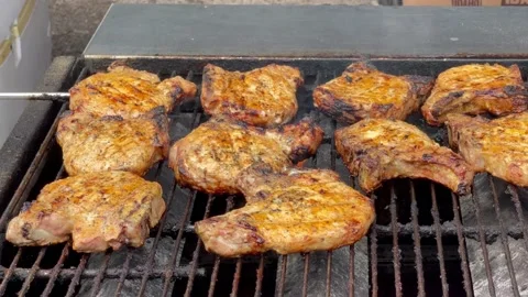 Close up slow pan of multiple pork chops on large open flame grill Stock Footage 239117712
