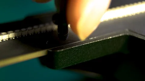 A close up of a small black screw being screwed into a holographic fan with a Stock Footage 96225557