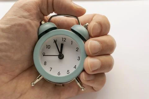 Close-up of a small blue alarm clock in man's hand. the time is 23-55 库存照片