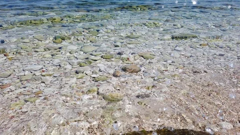 Close-up of small coastal waves rolling on sand, breaking on rocks in sun Stock Footage 122651927