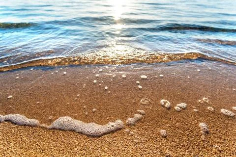 Close up of small sea waves with clear blue water over yellow sand beach at s Stock-Fotos