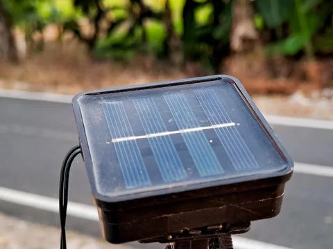 Close-up of a small solar panel with a blurred background of trees and a road Stock Photos