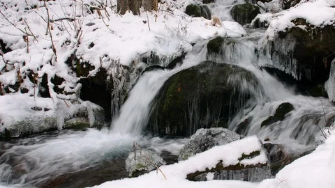 Close up of a small waterfall flowing over rocks and ice in a snow covered Vídeos de archivo 99722903