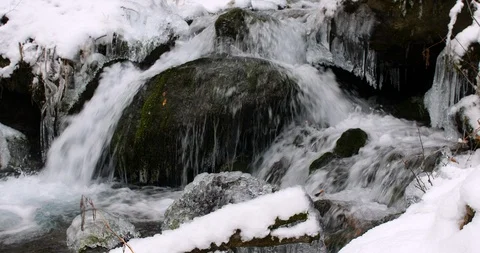 Close up of a small waterfall flowing over rocks and ice in a snow covered Vídeos de archivo 99722939