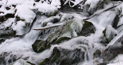 Close up of a small waterfall flowing over rocks and ice in a snow covered Vídeos de archivo 99723403