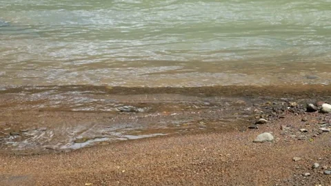 Close up of small waves crashing against the sand of the river bank Видео 336878030