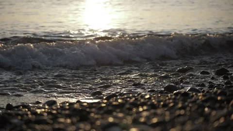 Close up of small waves hitting rocks at shore at sunset Stockbeeldmateriaal 277378403