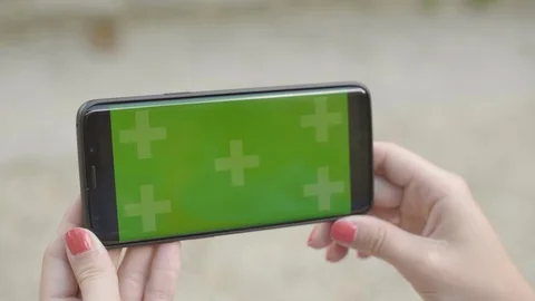 Close-up of smartphone with Green Screen Sitting on bench in park, holding by Видео 111926786