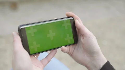 Close-up of smartphone with Green Screen Sitting on bench, holding by woman in Vídeos de archivo 111926912