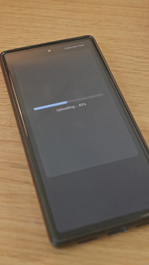Close-up of smartphone lying on wooden table showing data uploading progress Stock Footage 341860560