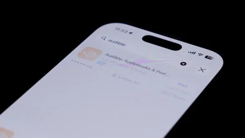 Close-up of a smartphone screen showing the Audible app being searched Stock Footage 334062930