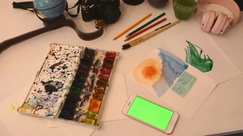 Close up smartphone on table with art objects watercolor brush studio art home Stock Footage 113335490