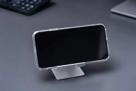 Close-up of a smartphone with a transparent case sits on a metal stand on a.. Stock Photos