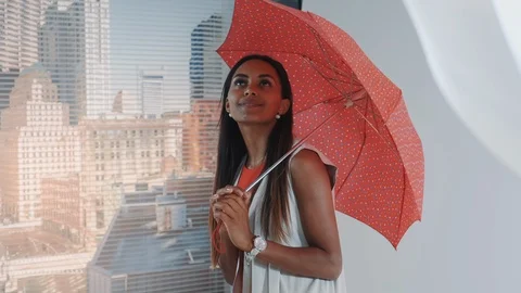 Close-up of smiling black model posing with red umbrella on bar high chair for Vídeos de archivo 122586847
