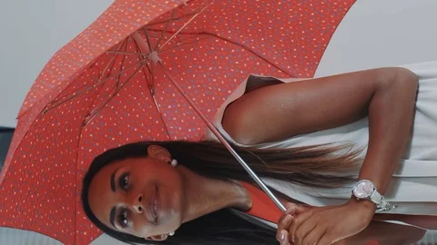 Close-up of smiling black model posing with red umbrella on bar high chair for Stock Footage 129881401