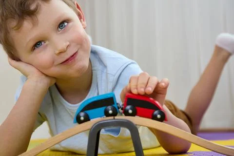 Close up smiling boy is having fun playing with wooden toys on puzzle mats Stock Photos