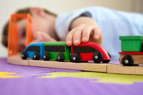 Close up smiling boy is having fun playing with wooden toys on puzzle mats Stock Photos