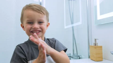 Close up of smiling child in a gray t-shirt soaps his hands and looking at the Stock Footage 131160640